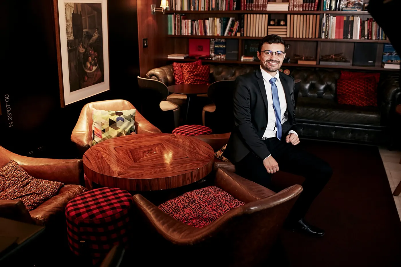 Diego Voloski sentado em uma sala com estantes de livros e poltronas de couro